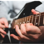 Palm muting guitar strings on a black electric guitar.