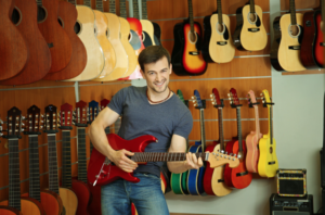 A guy smiling playing a red electric guitar at a music store.