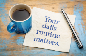 A wooden table with a cup of coffee, a pen and piece of paper on it. Written on the paper is Your daily routine matters.