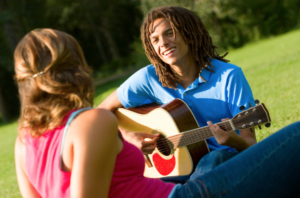 A man strumming an acoustic guitar facing a woman.