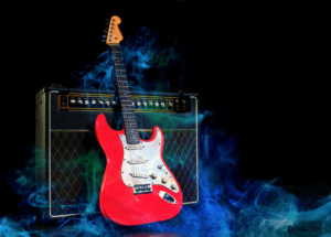 A red electric guitar leaning up against an amplifier.